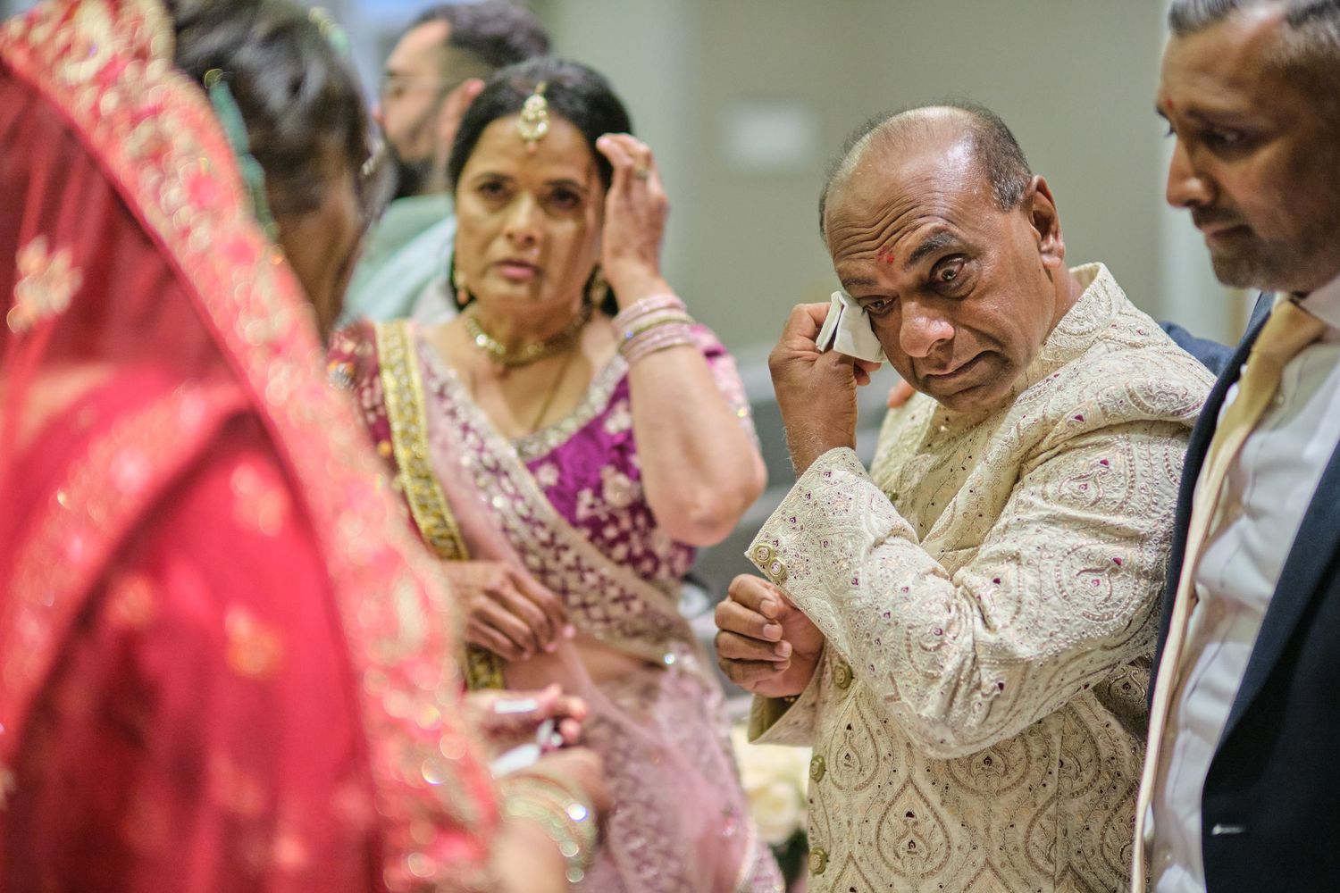 Wedding guests share joyful moments during an elegant indoor reception with warm lighting and traditional attire.