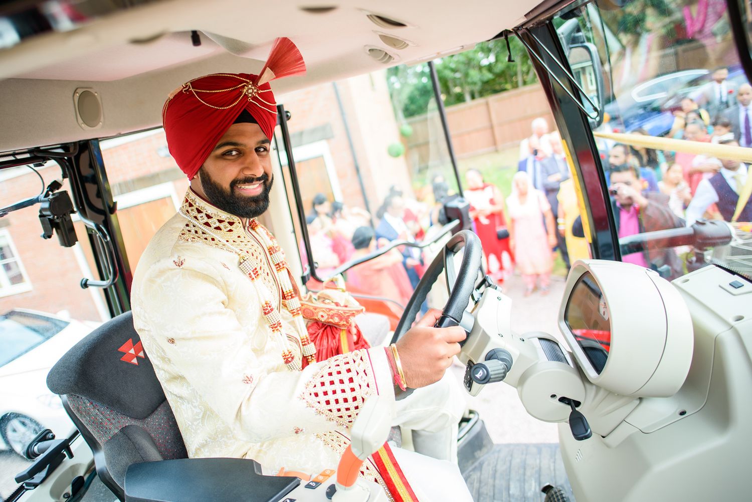 Traditional Indian groom in formal attire sitting in driver's seat of a decorated vehicle.