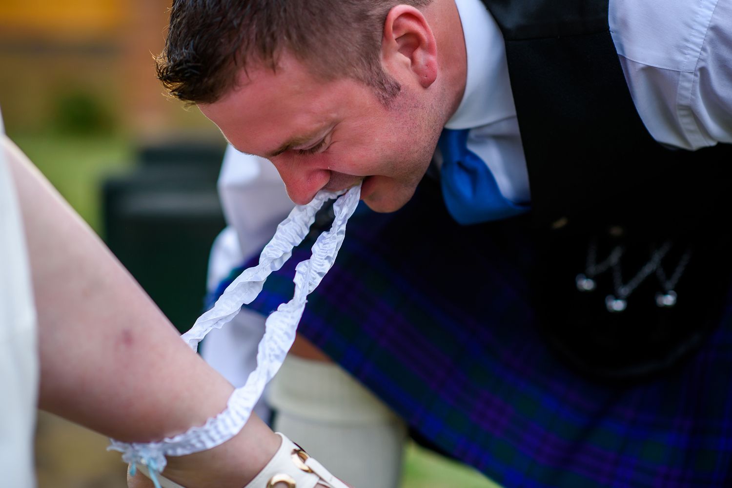 Scottish wedding guests in kilts perform traditional dance moves at an outdoor reception.