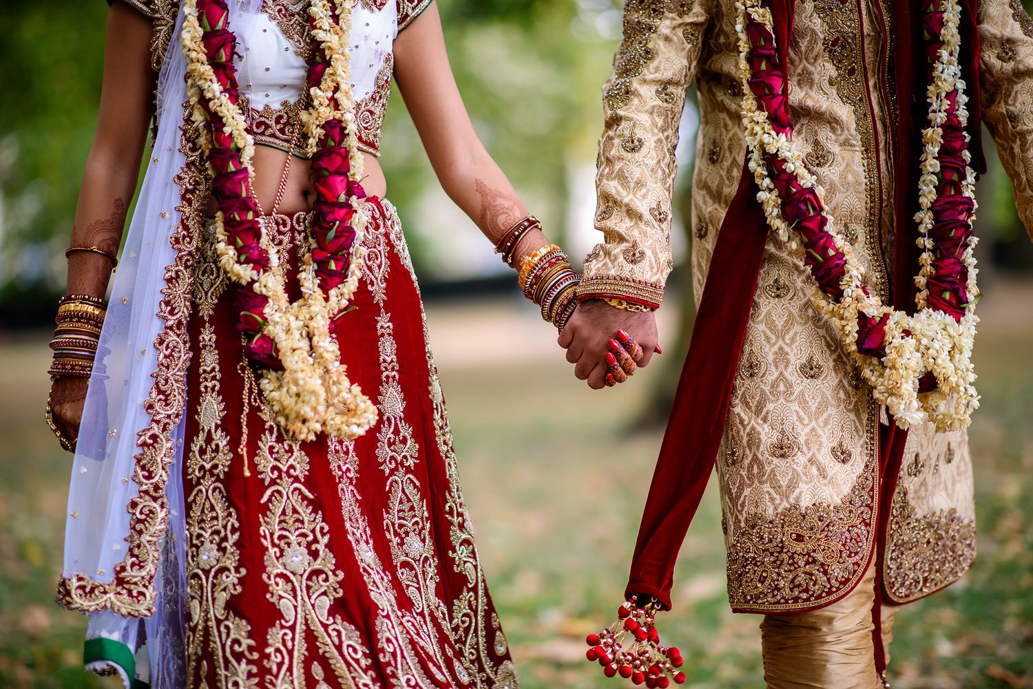 Traditional Indian wedding couple photographed with ornate red and gold garlands.