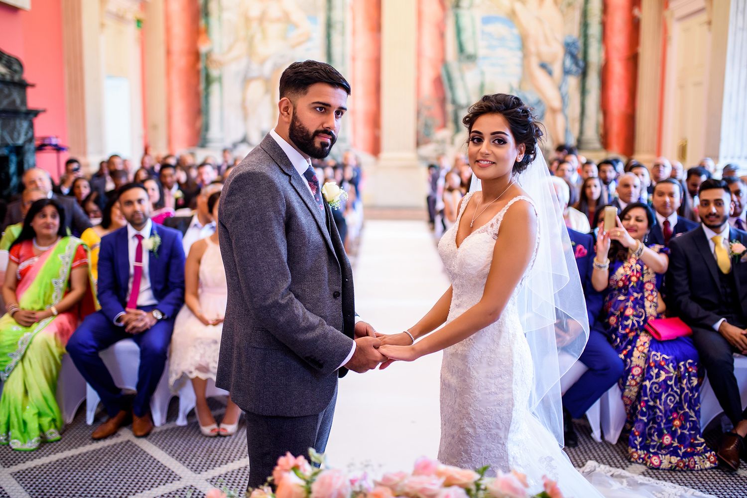 Festive wedding celebration with guests in colorful attire against coral walls.