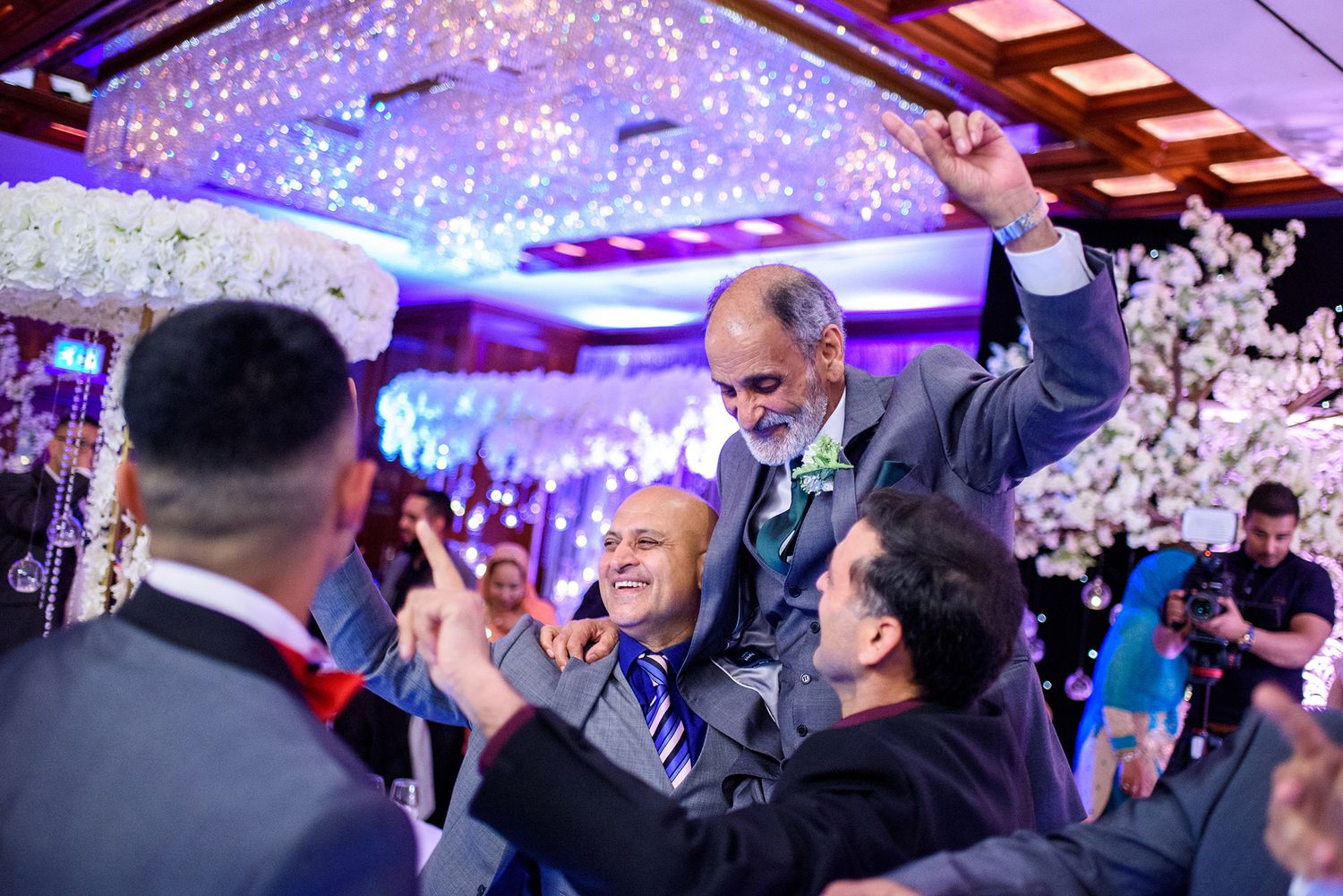 Festive wedding reception scene with purple uplighting and people celebrating on dance floor.