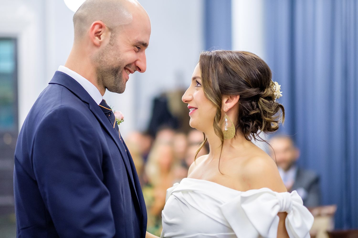 Intimate wedding moment captured in front of blue curtains and natural lighting.