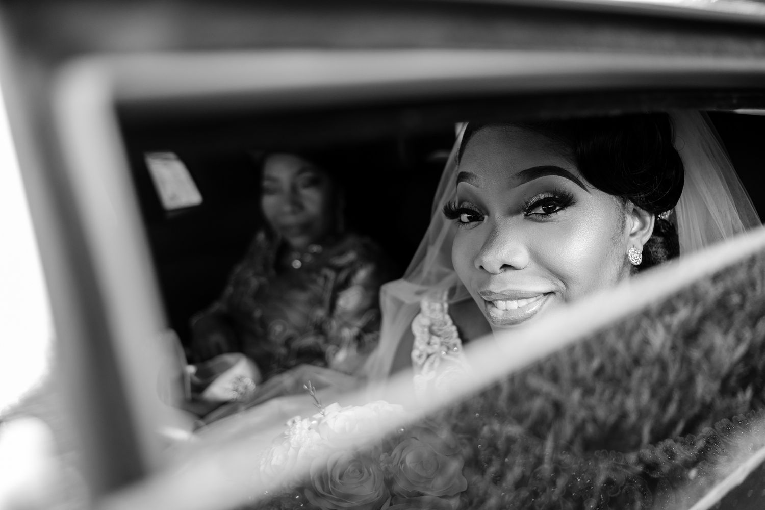 A wedding couple sits in a car seen through windows and reflections.