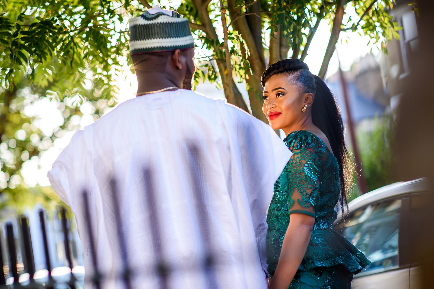 An elegant couple poses for outdoor portraits against a backdrop of trees and sunlight.