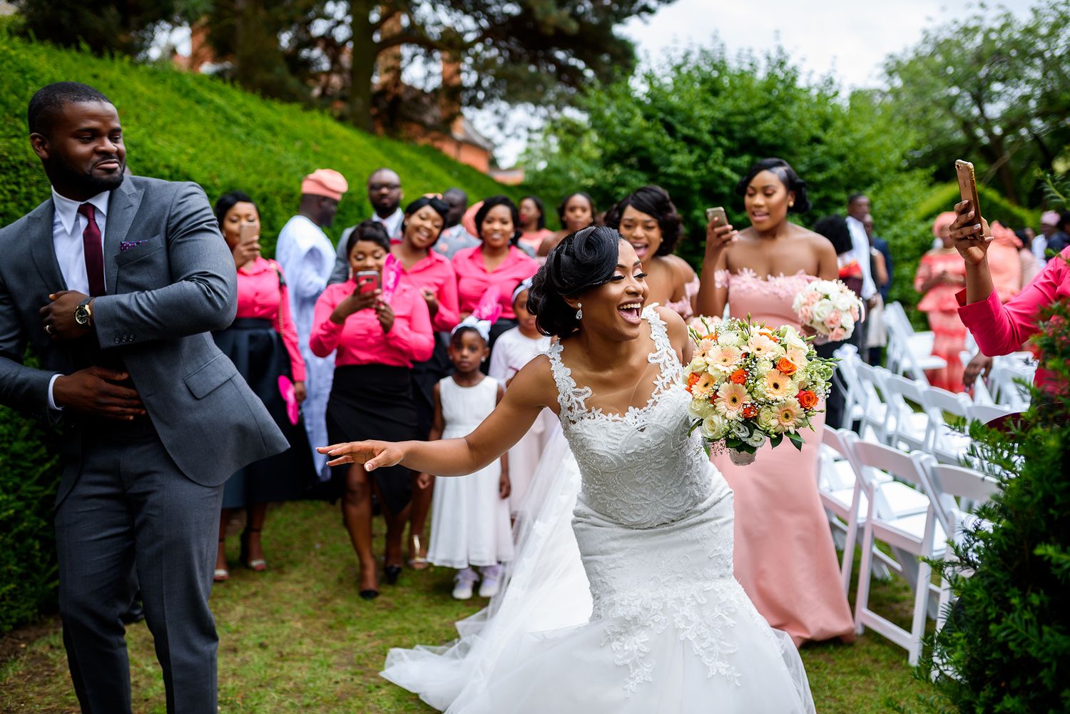 Outdoor wedding reception shows guests and wedding party dancing and celebrating on a green lawn.