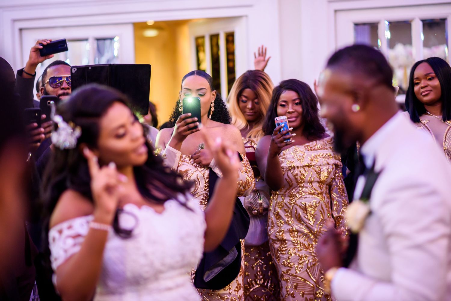 Wedding reception dance floor filled with guests in formal attire celebrating under purple lighting.