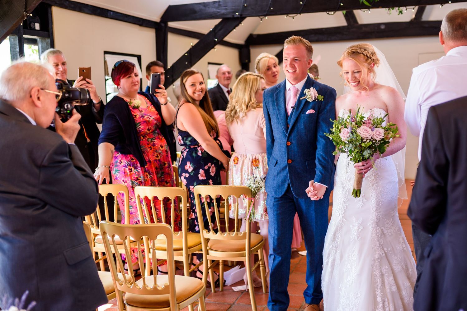 Wedding guests seated in wooden chairs during an indoor ceremony with natural lighting.