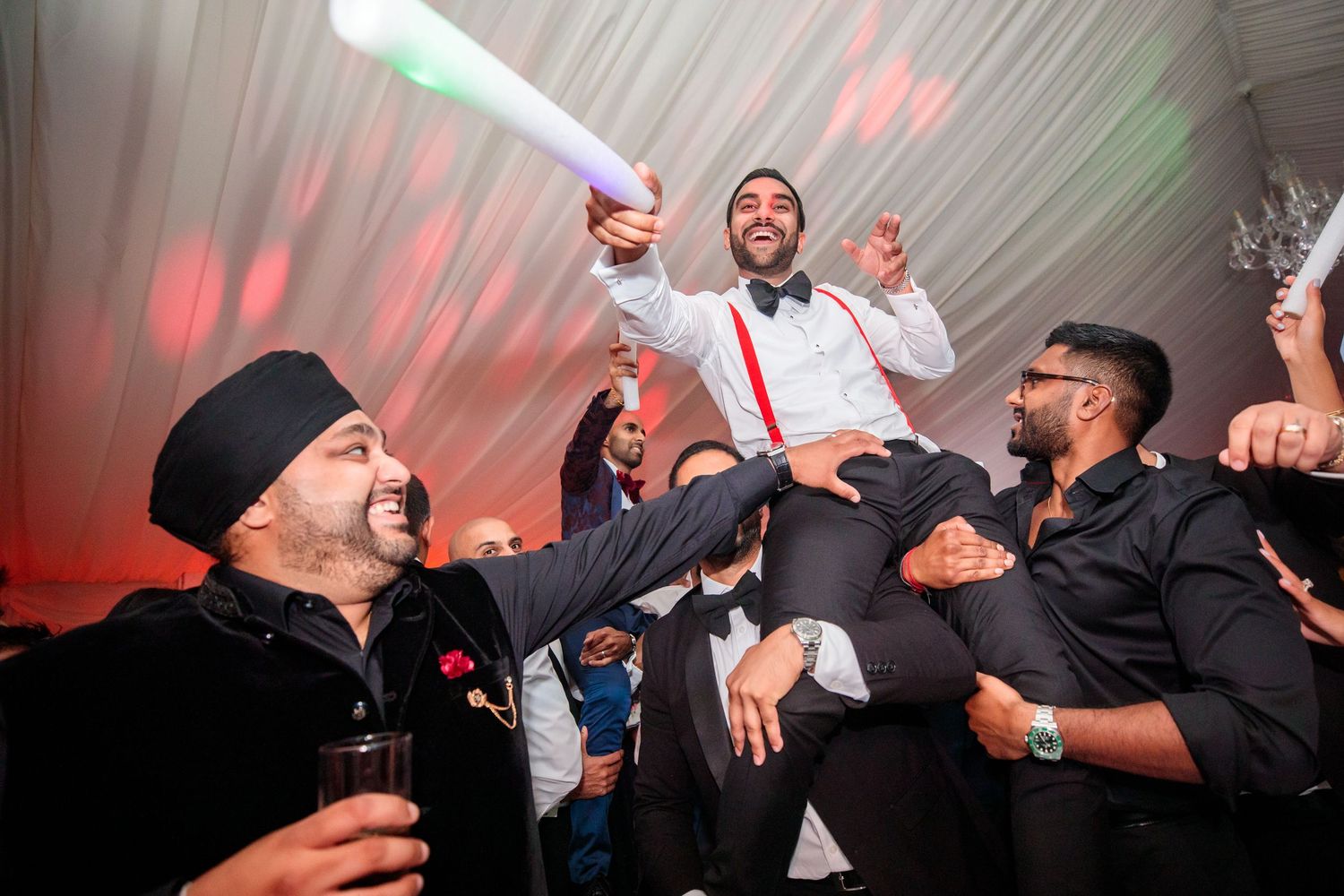 Wedding party dancing and celebrating under dramatic red lighting at reception.