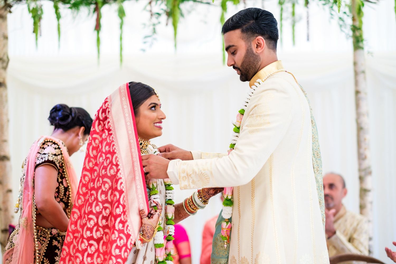 Wedding guests celebrate during an outdoor ceremony with hanging floral decorations and white drapes.