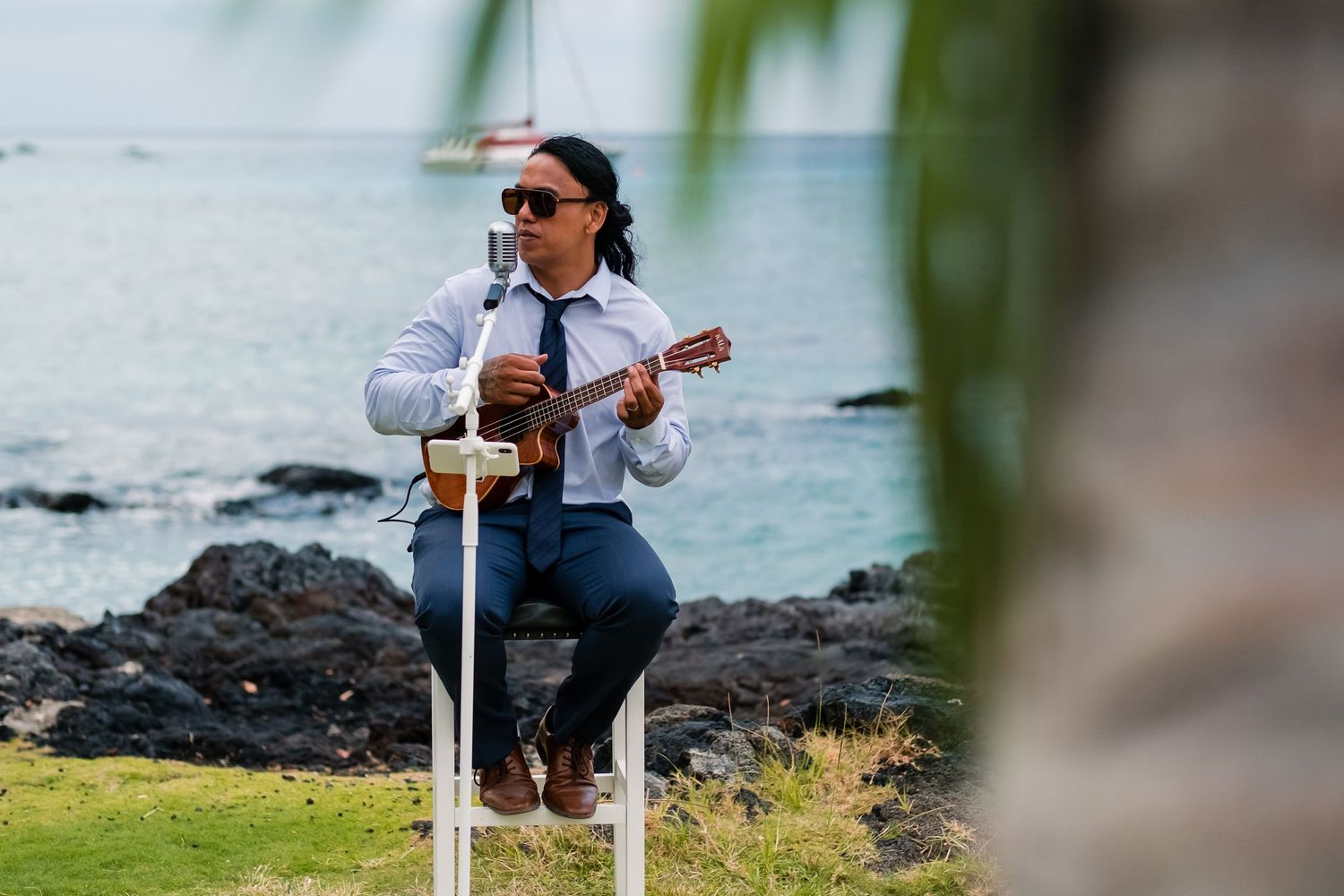 Musician performs with ukulele on rocky oceanfront setting in Hawaii.