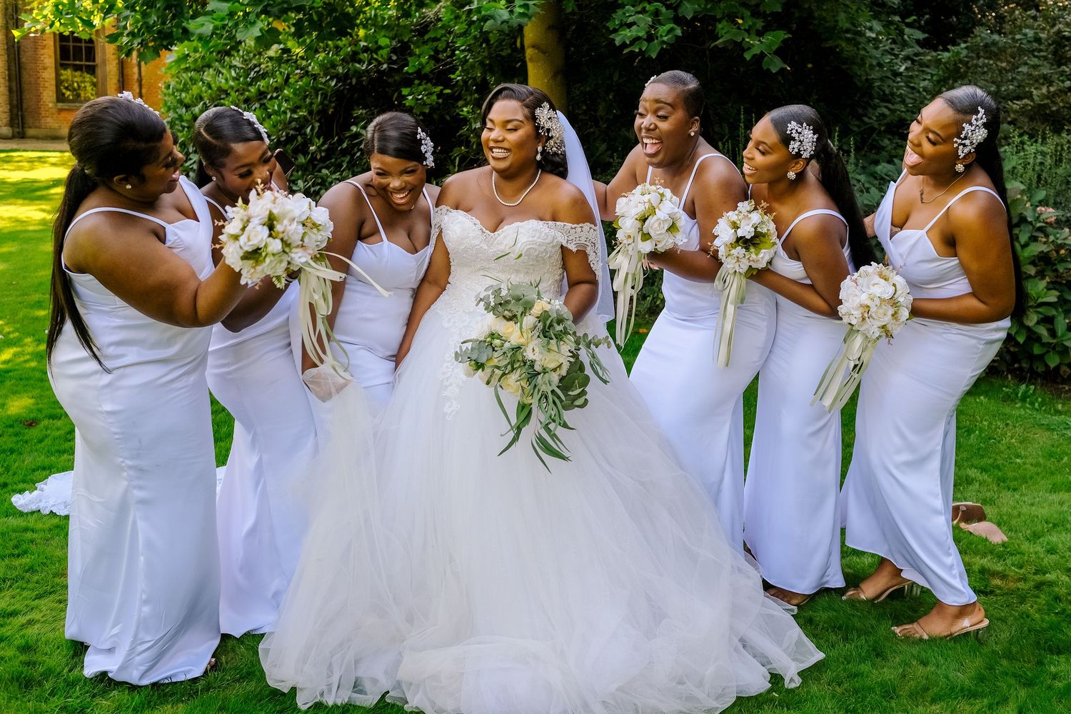 A bride in a flowing white gown celebrates with her bridesmaids holding bouquets in a garden setting.