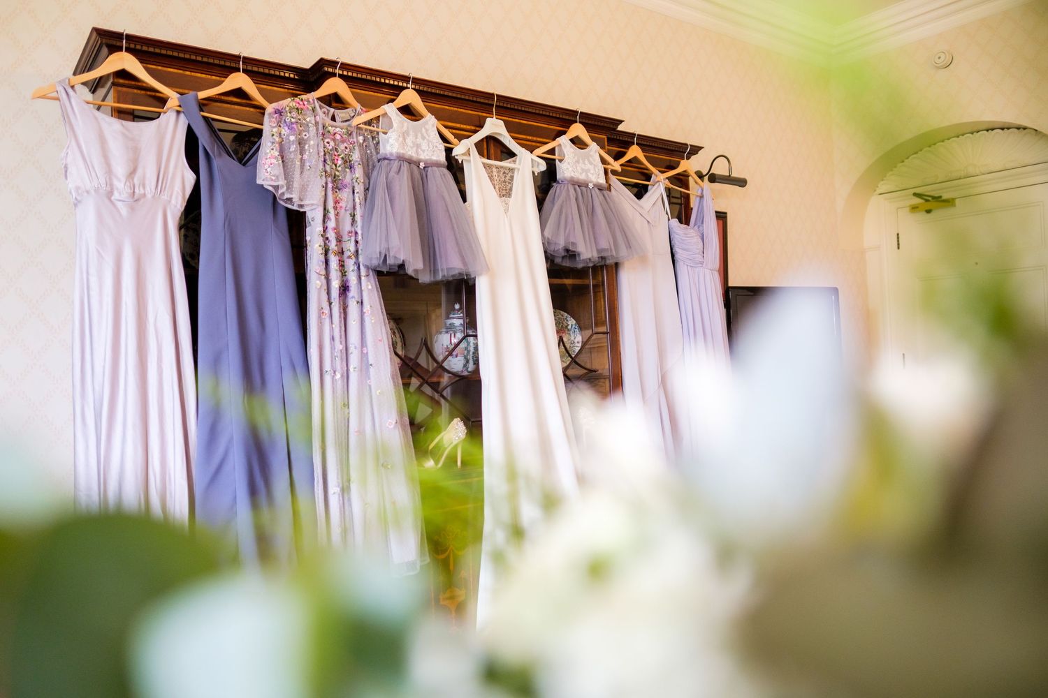 Elegant white dresses and formal wear hanging on wooden hangers in a boutique clothing store display.