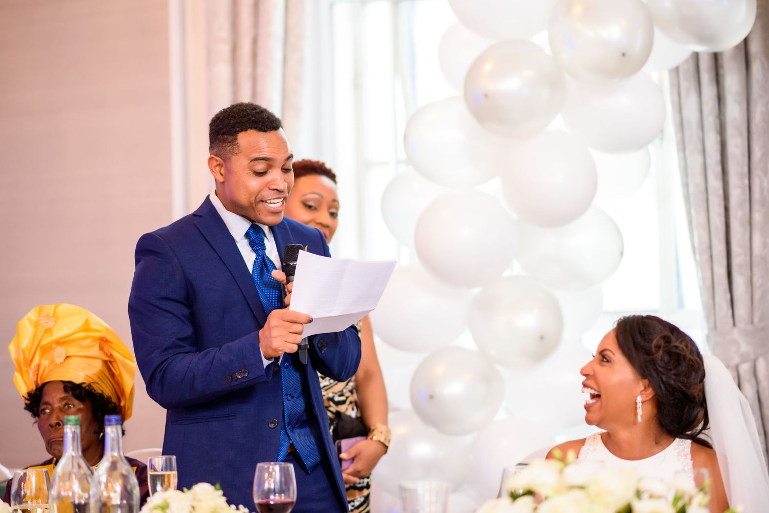Wedding reception in elegant ballroom with white balloon decorations and guests in formal attire.