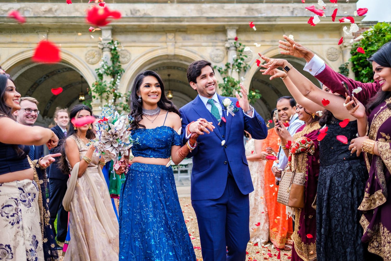 Wedding celebration with guests throwing confetti as couple walks through crowd at historic building entrance.