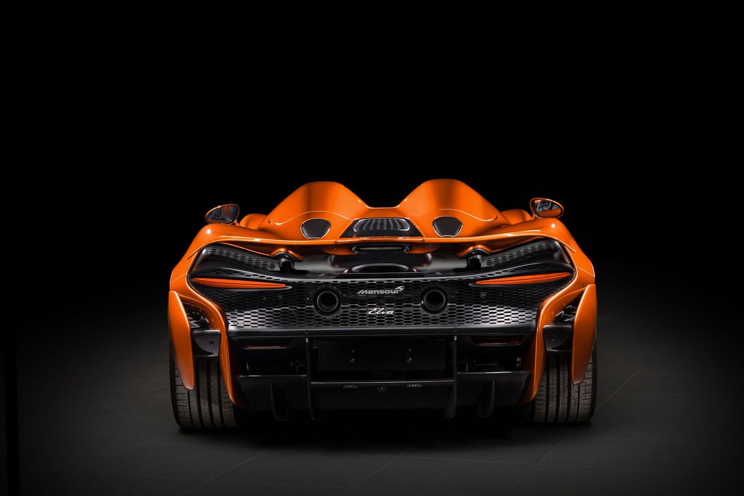 Rear view of an orange McLaren supercar showcasing its aggressive aerodynamic design against a dark background.