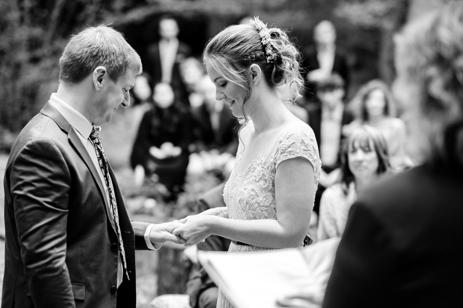 Black and white photo of an intimate outdoor wedding ceremony in a forest setting.