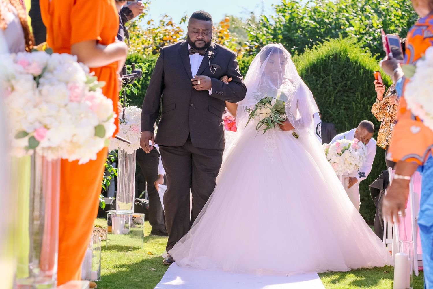 Wedding ceremony outdoors with bridesmaids in vibrant orange dresses standing in a row.