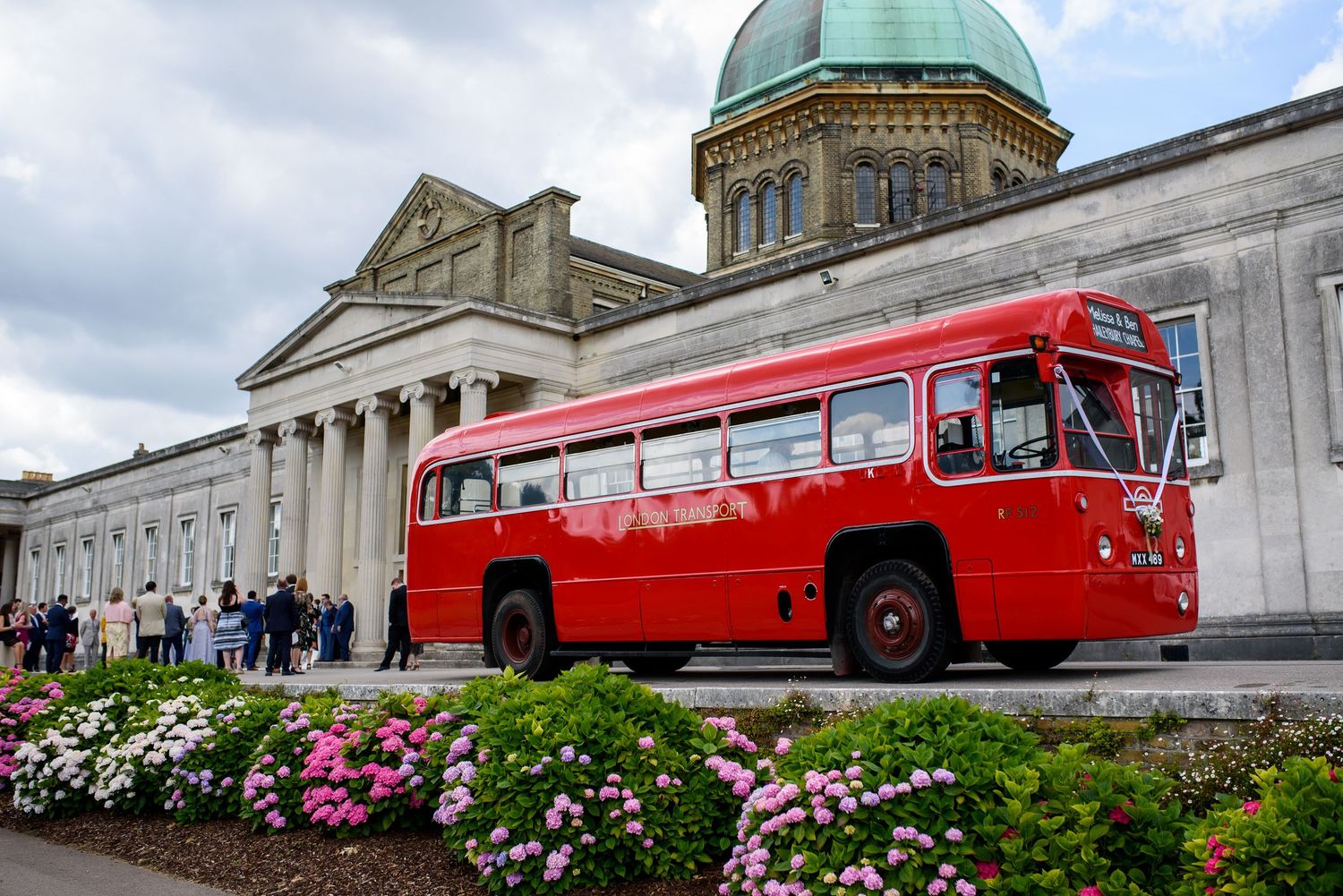 Red vintage streetcars and historic buildings line up against a cloudy sky with pink flowers in the foreground.