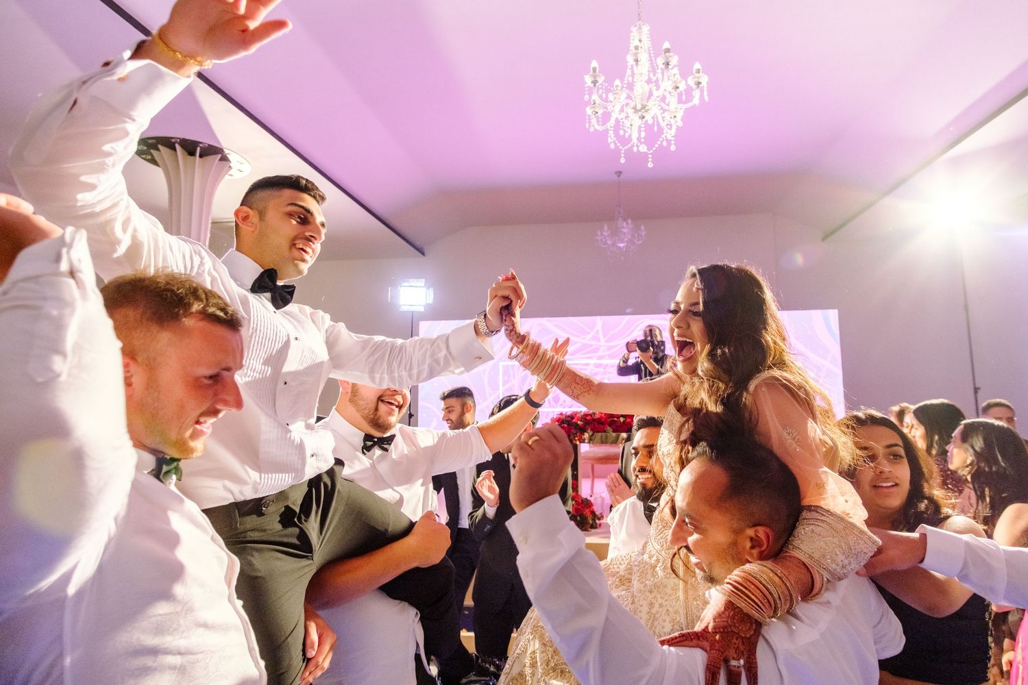 Wedding reception party with energetic dancing and celebration under purple-lit ceiling.