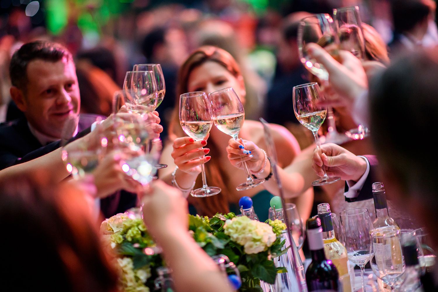 People raise wine glasses in a celebratory toast during an elegant dinner gathering.