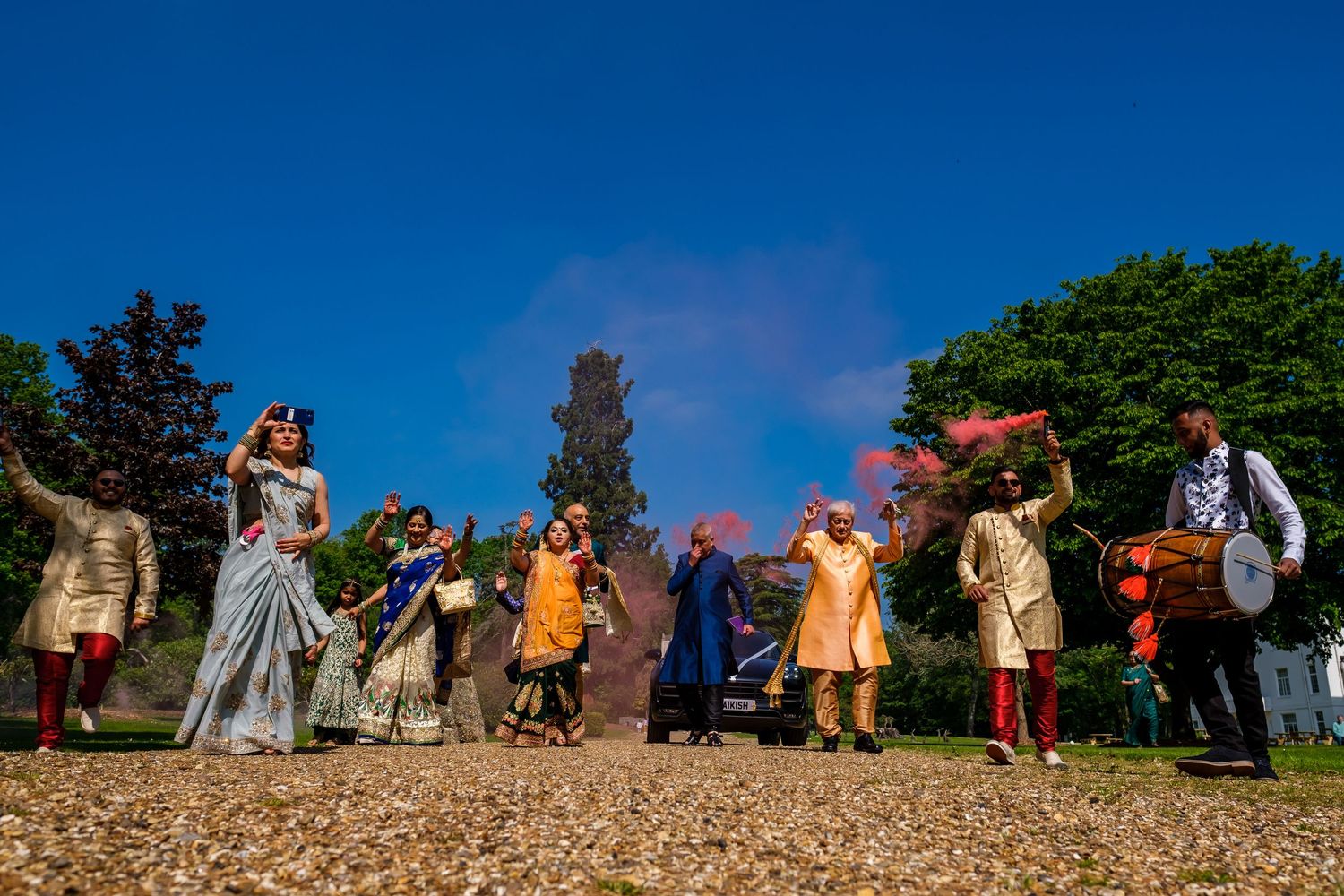 Wedding party poses on hillside with colorful smoke effects during outdoor celebration.