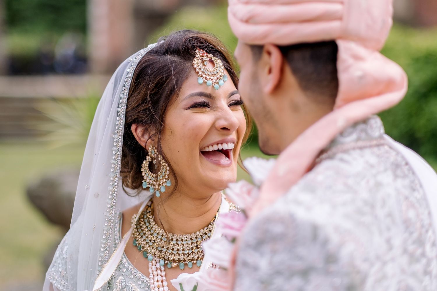 Bride in traditional Indian jewelry and veil shares intimate moment during wedding celebration.