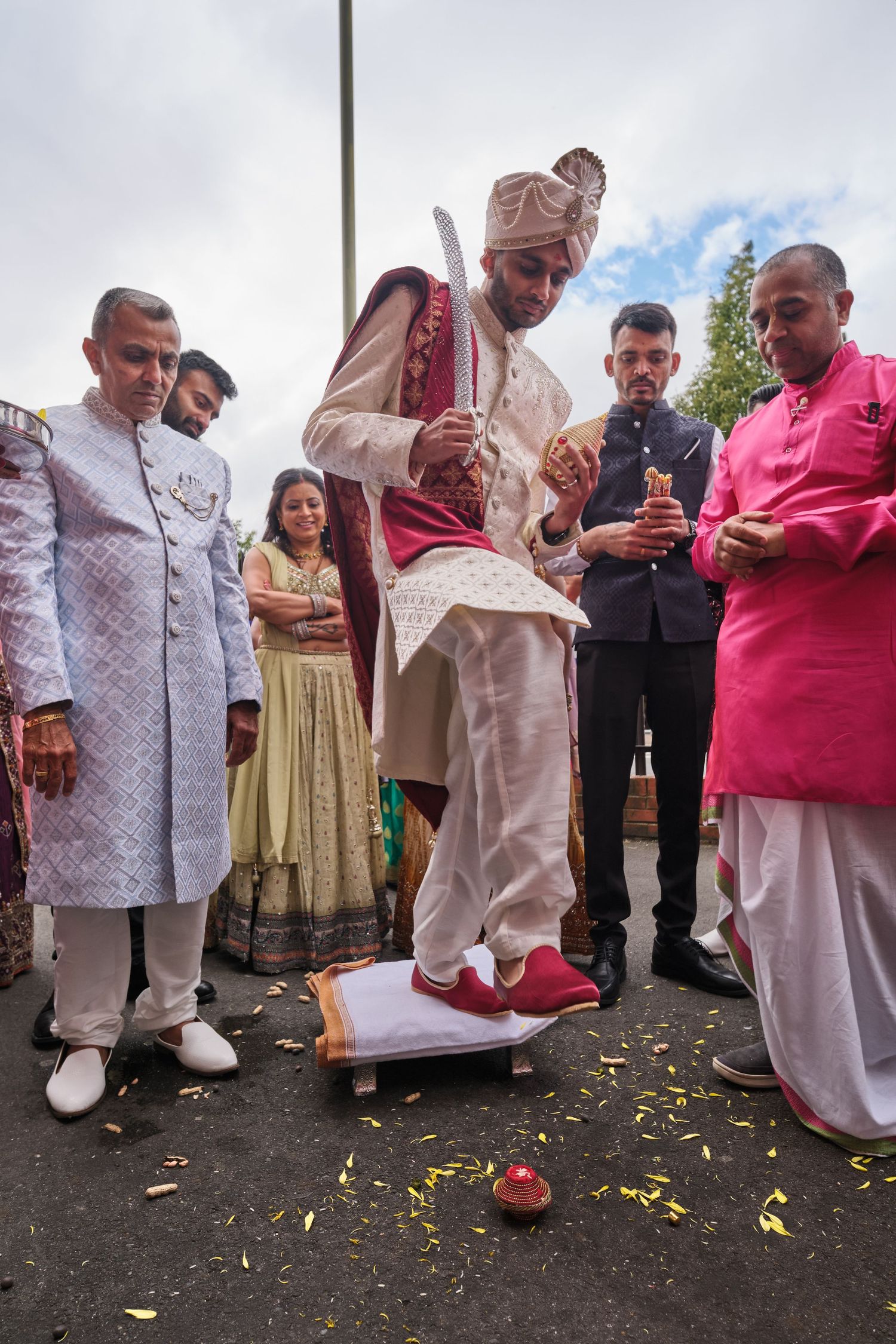 Group of people in traditional attire participating in a cultural ceremony with scattered flower petals on ground.