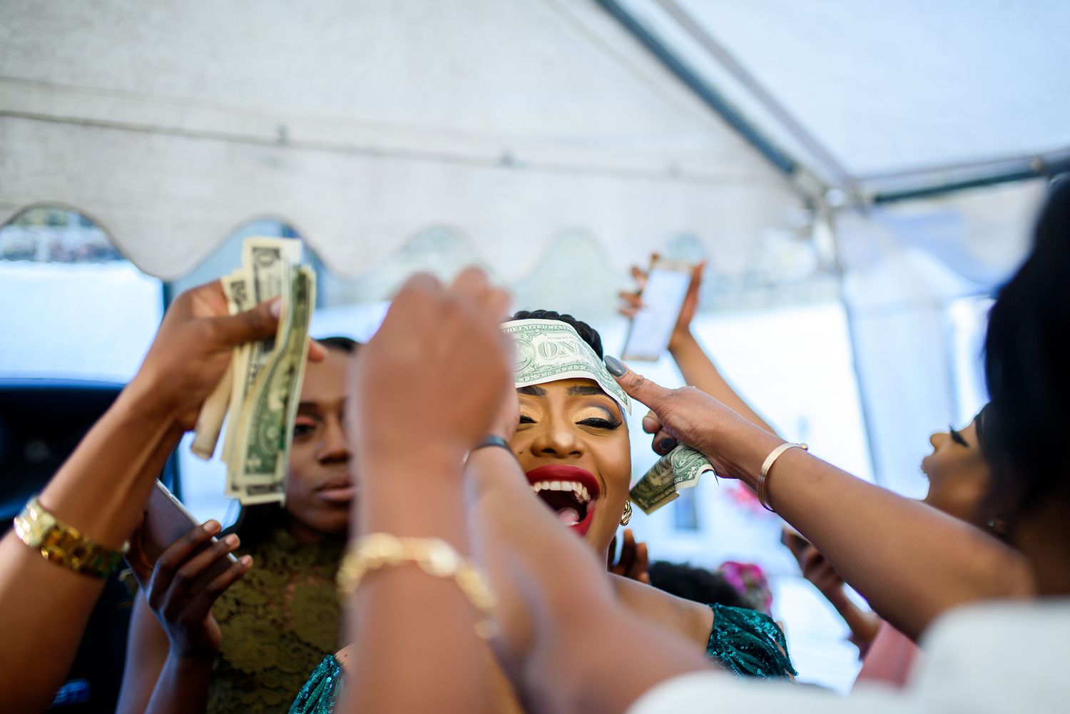People raising their hands in celebration under a white tent canopy during a party.
