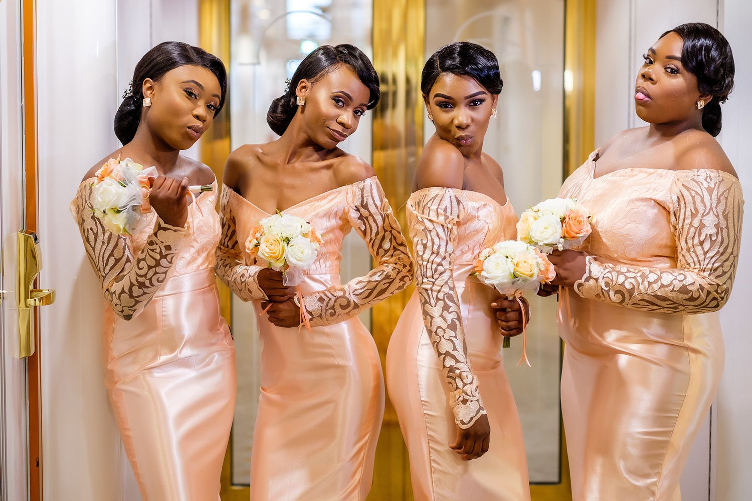 Group wearing peach-colored satin dresses with lace details in an elegant indoor setting.