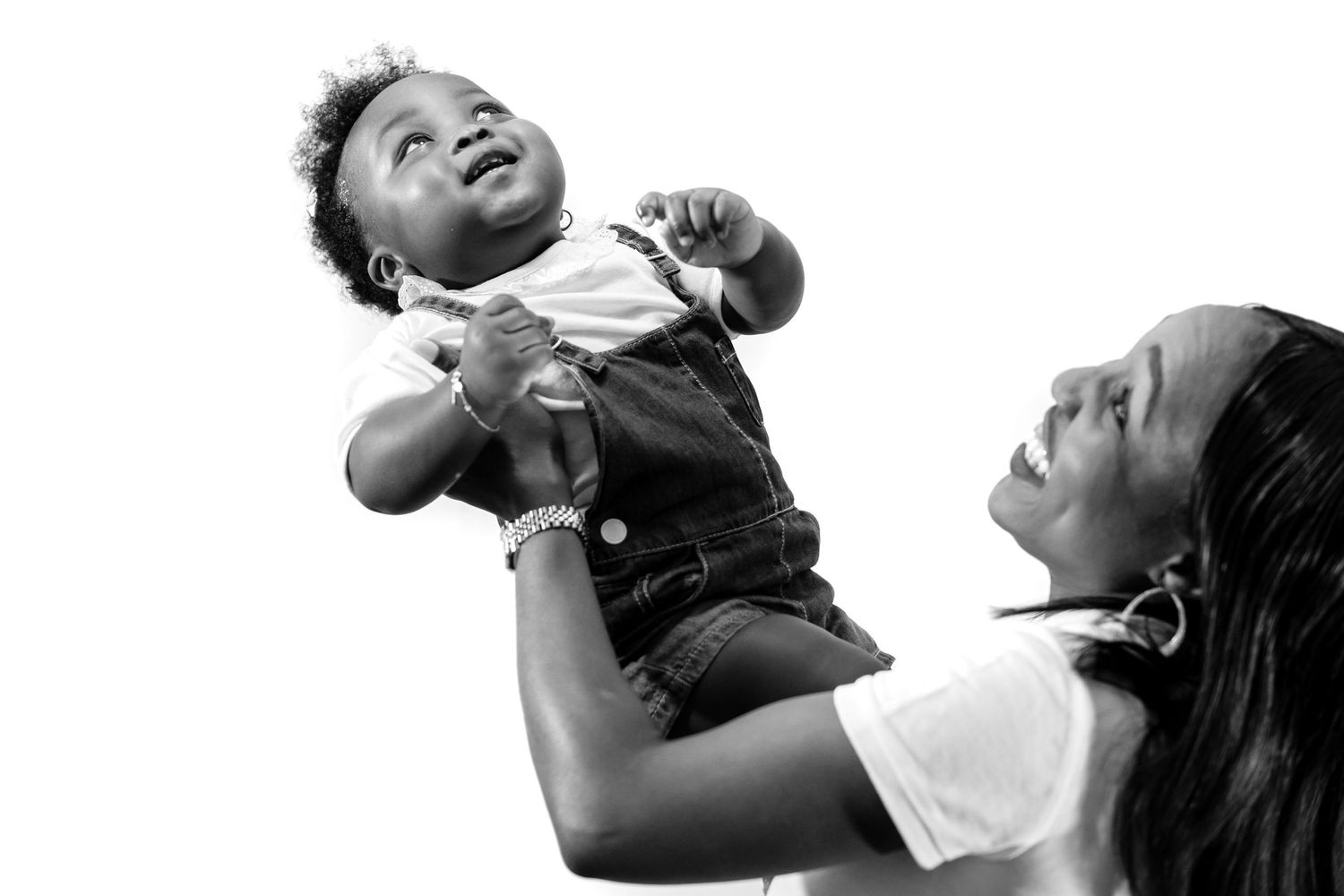 A joyful moment captured in black and white as a toddler is lifted high into the air with expressions of delight.