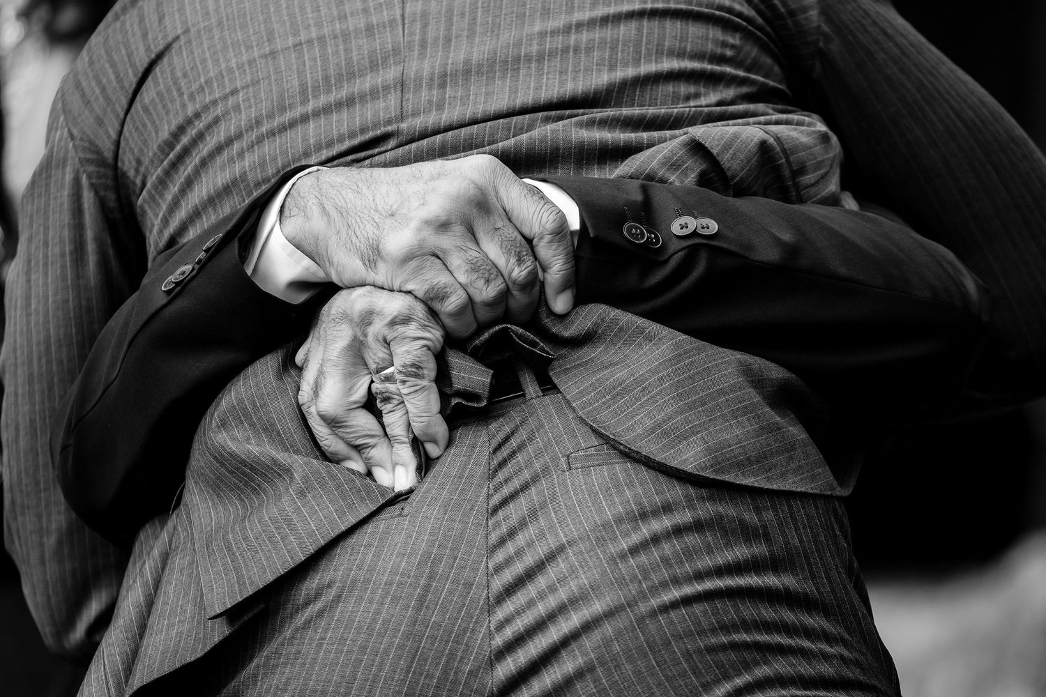 A person smooths and adjusts a gray pinstripe suit with two hands while standing up.