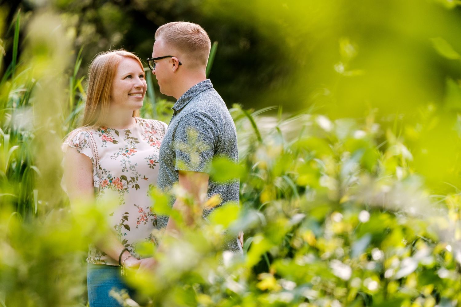 Couple sharing a romantic moment among green foliage in a sun-dappled garden.