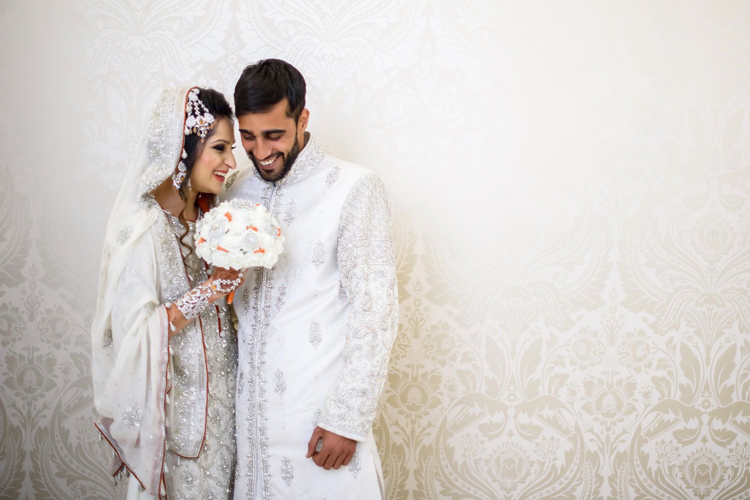 Couple in matching white traditional wedding attire sharing a tender moment.