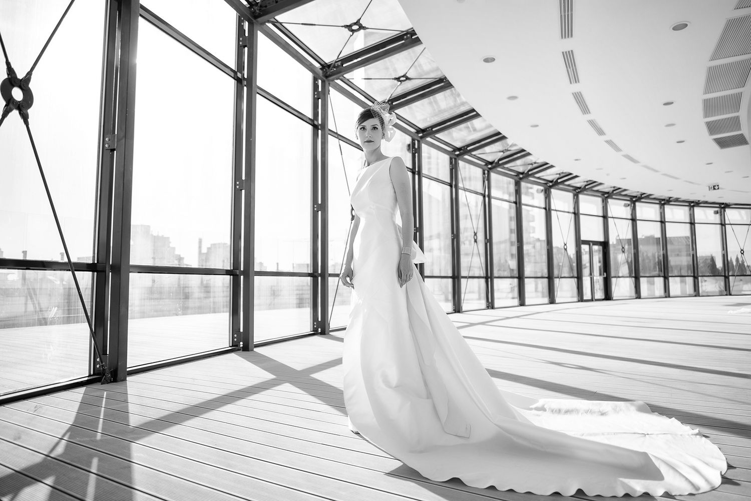 Wedding couple silhouetted in a modern glass-walled corridor with dramatic natural lighting.