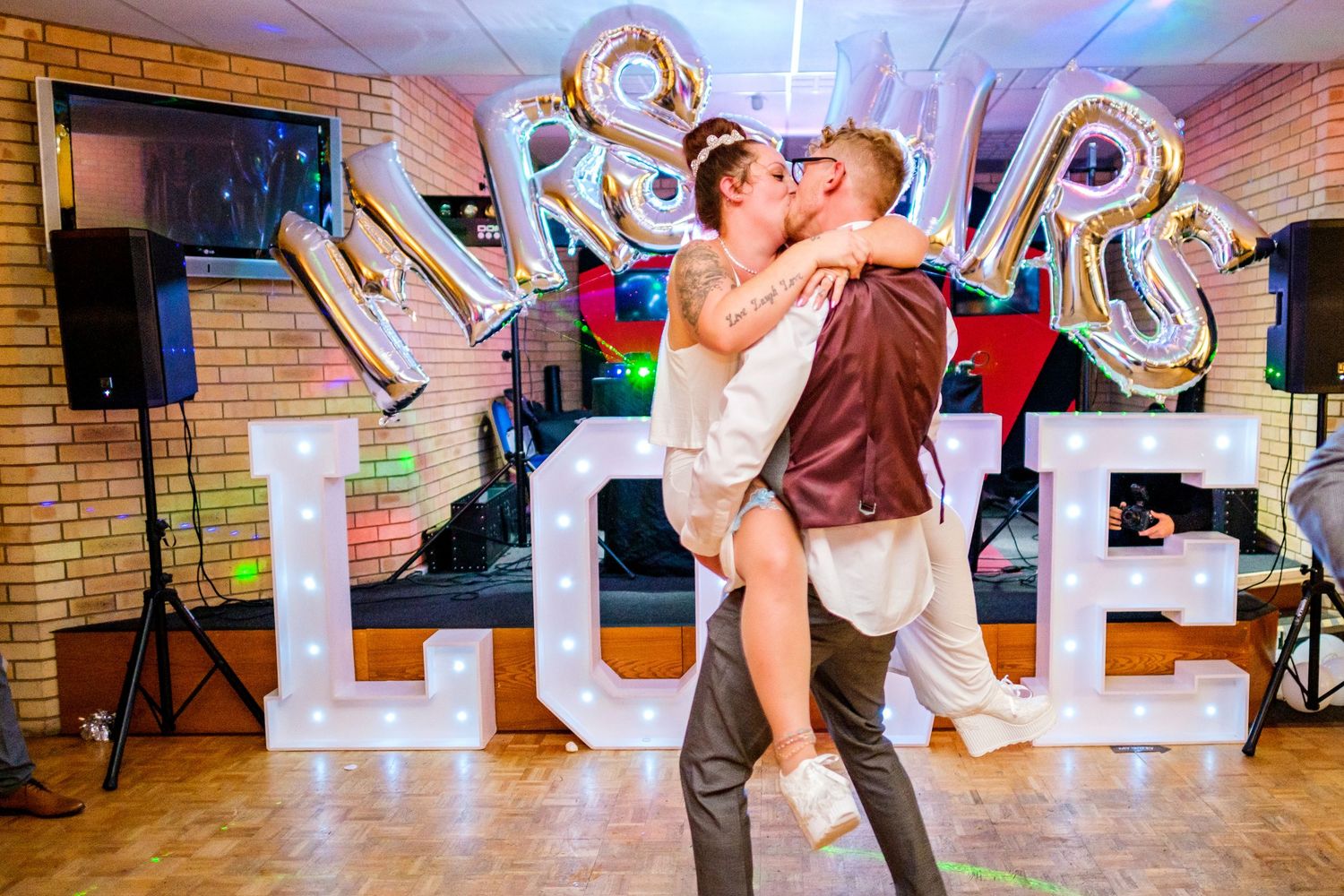 Wedding reception dance floor with colorful lights and balloon decorations in a brick-walled venue.