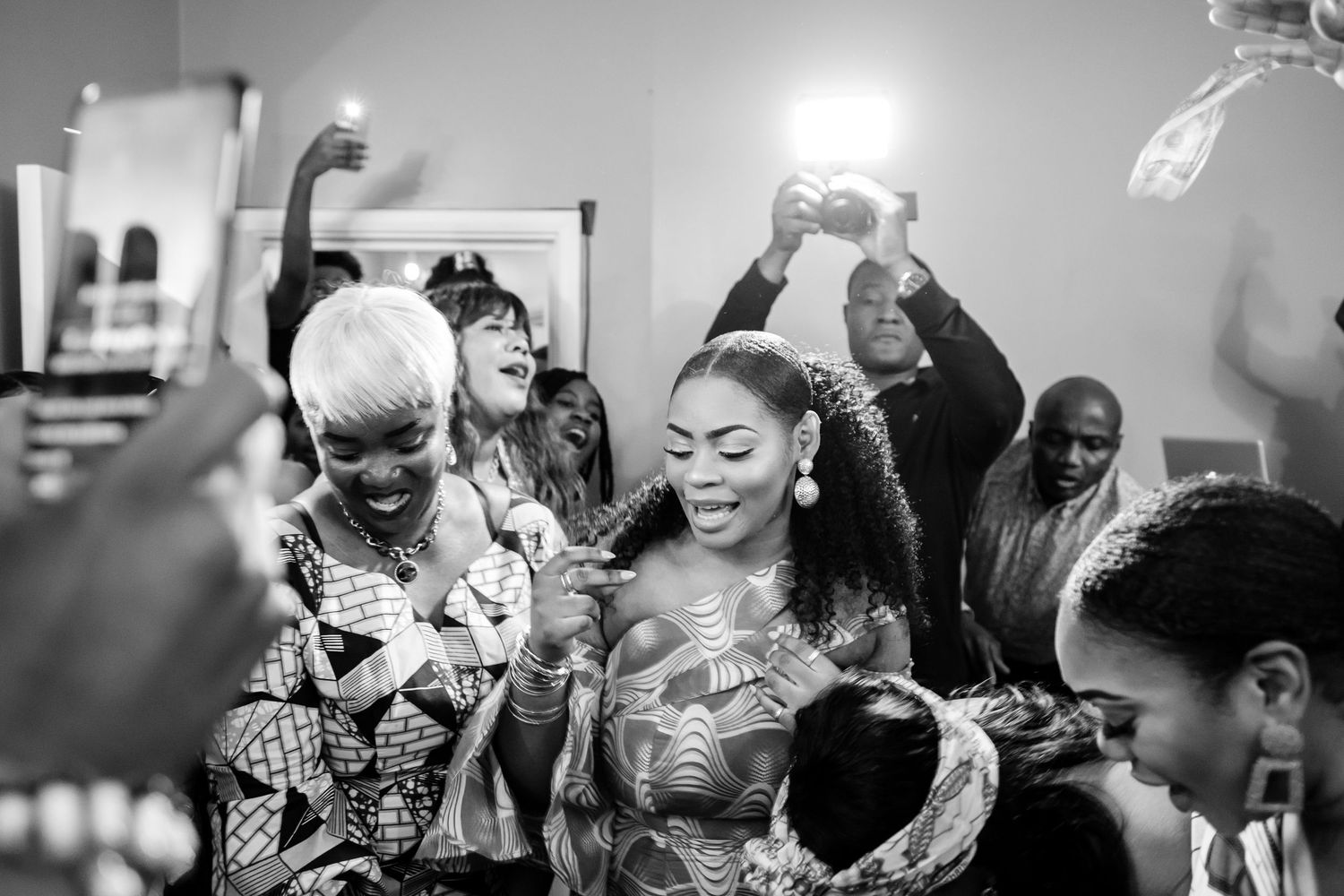 A joyous crowd celebrating at a party with raised hands and phones capturing the festive moment in black and white.