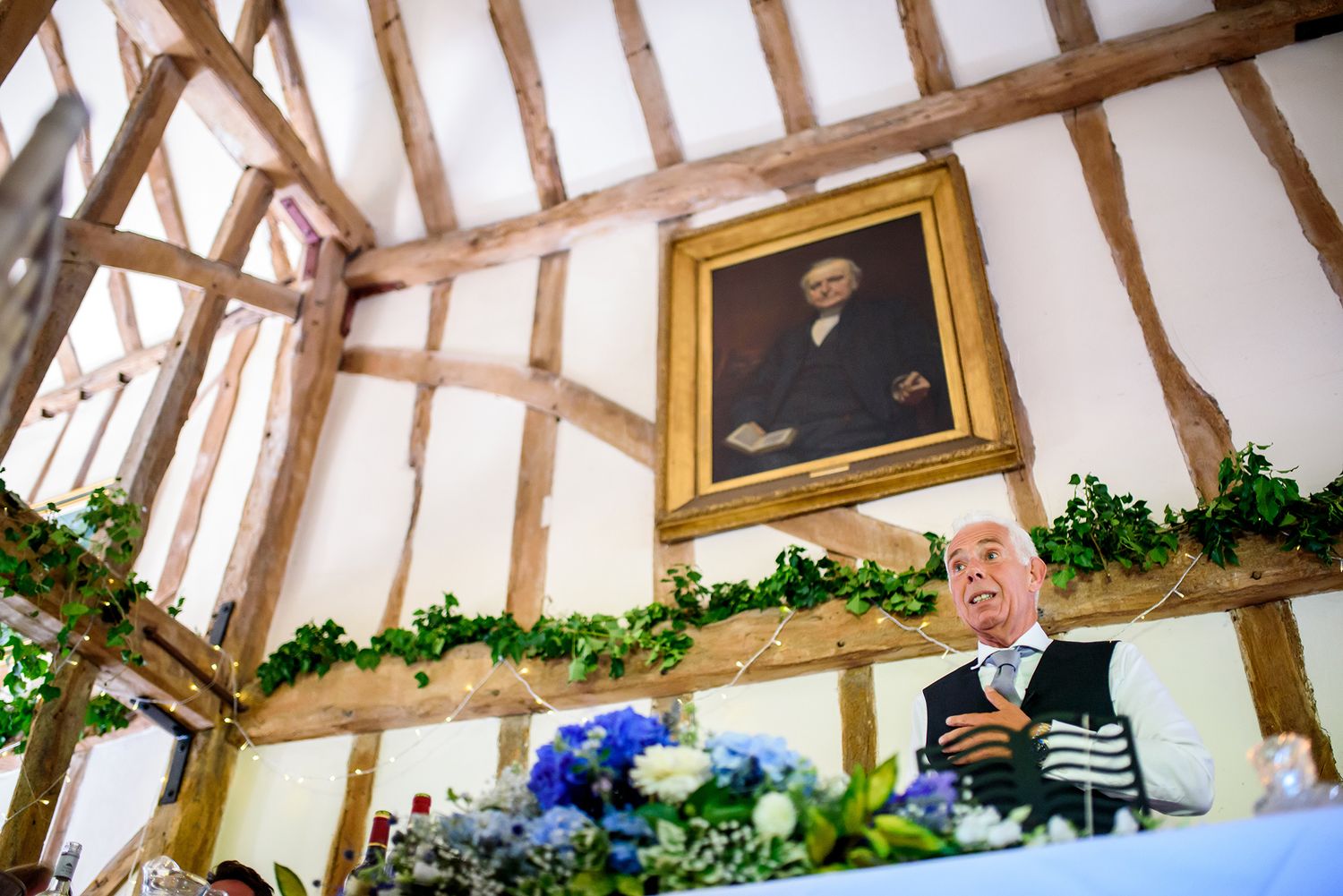 Rustic wooden beams and portrait frames decorate an indoor venue with greenery garlands.