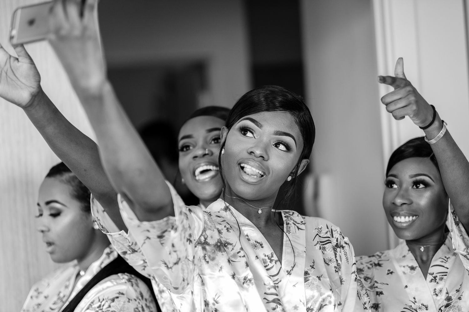 Group of bridesmaids in matching floral robes share excitement during morning preparations.