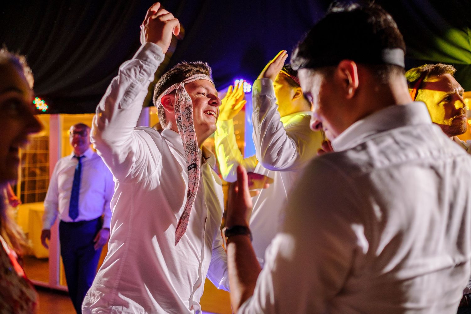 People dancing and celebrating at a nighttime party with colorful lighting effects.