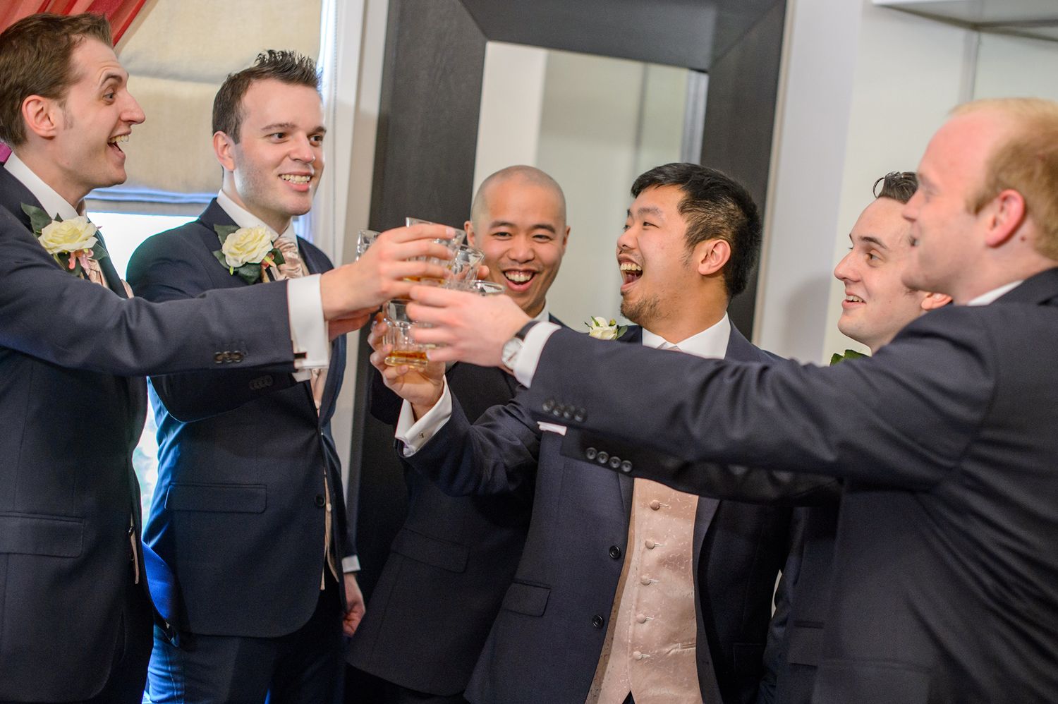 Group of groomsmen in suits celebrating with enthusiastic high fives.