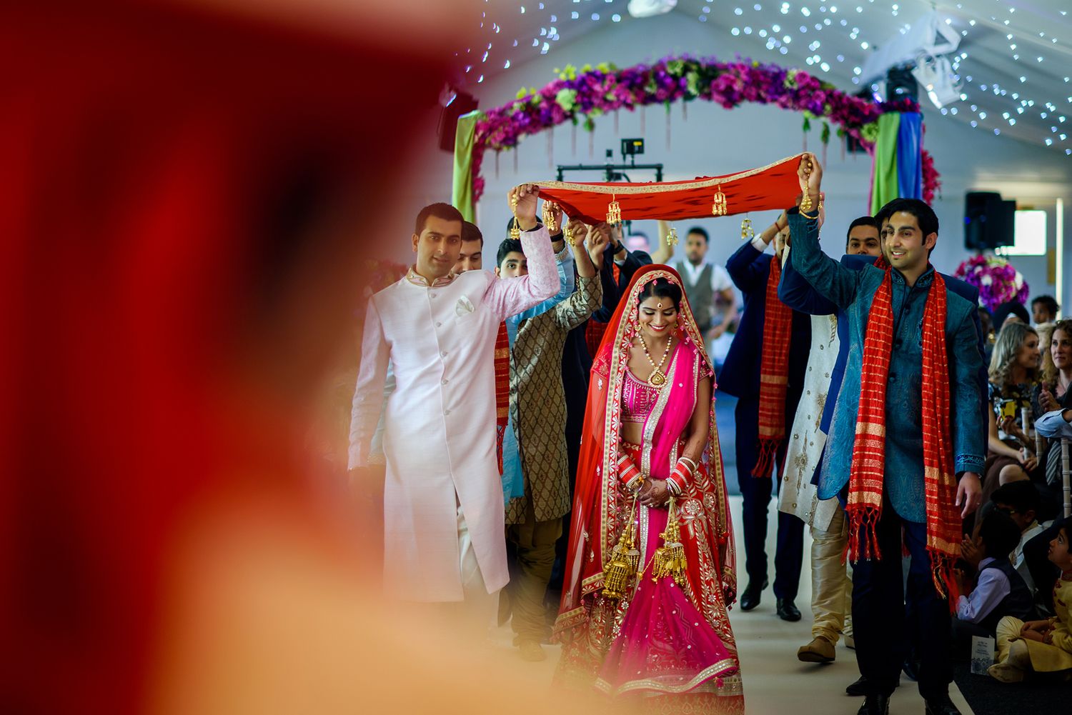 Wedding procession under decorated archway with sparkling lights and vibrant decorations.