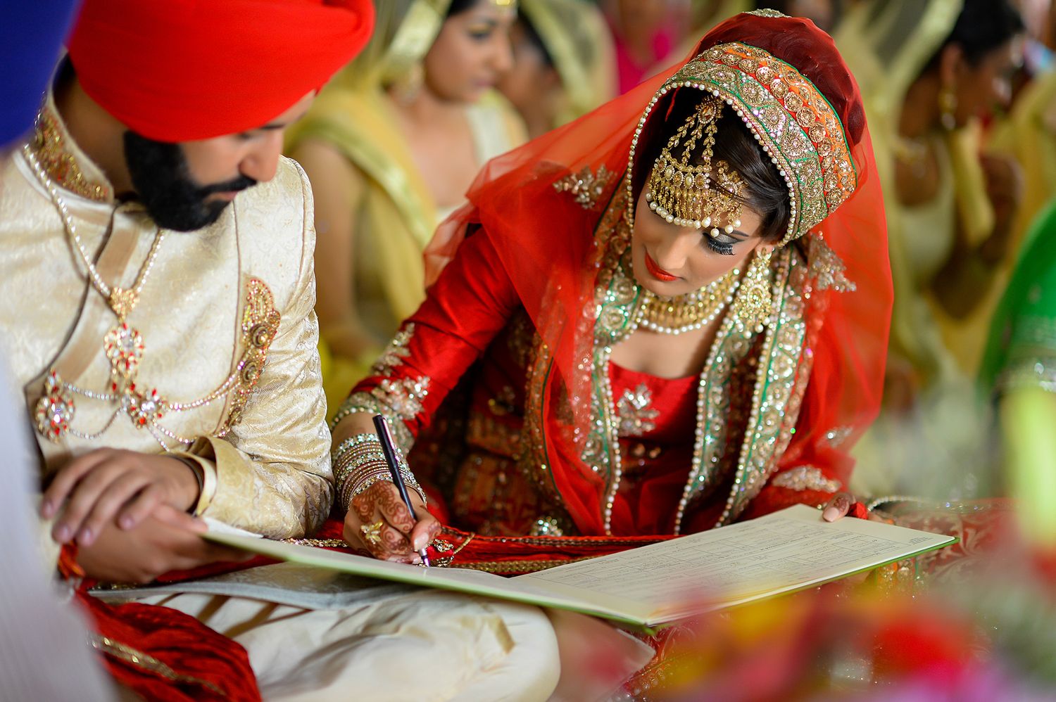Bride in red traditional dress signs wedding documents during Sikh ceremony.