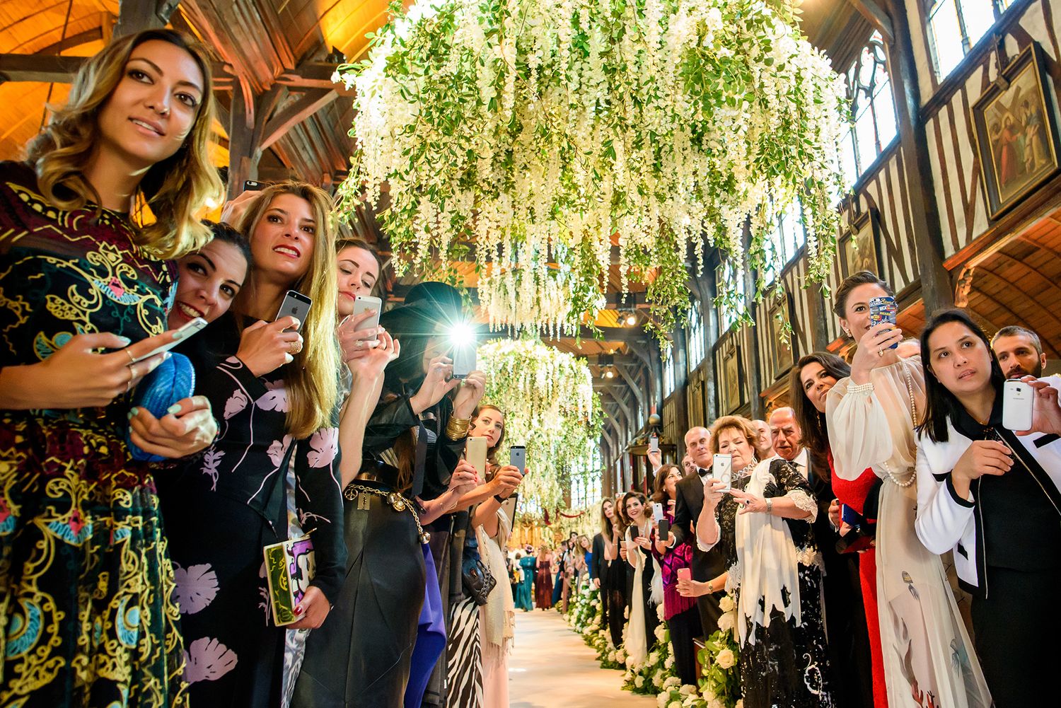 Wedding celebration in a grand hall with cascading floral decorations and natural light streaming through windows.