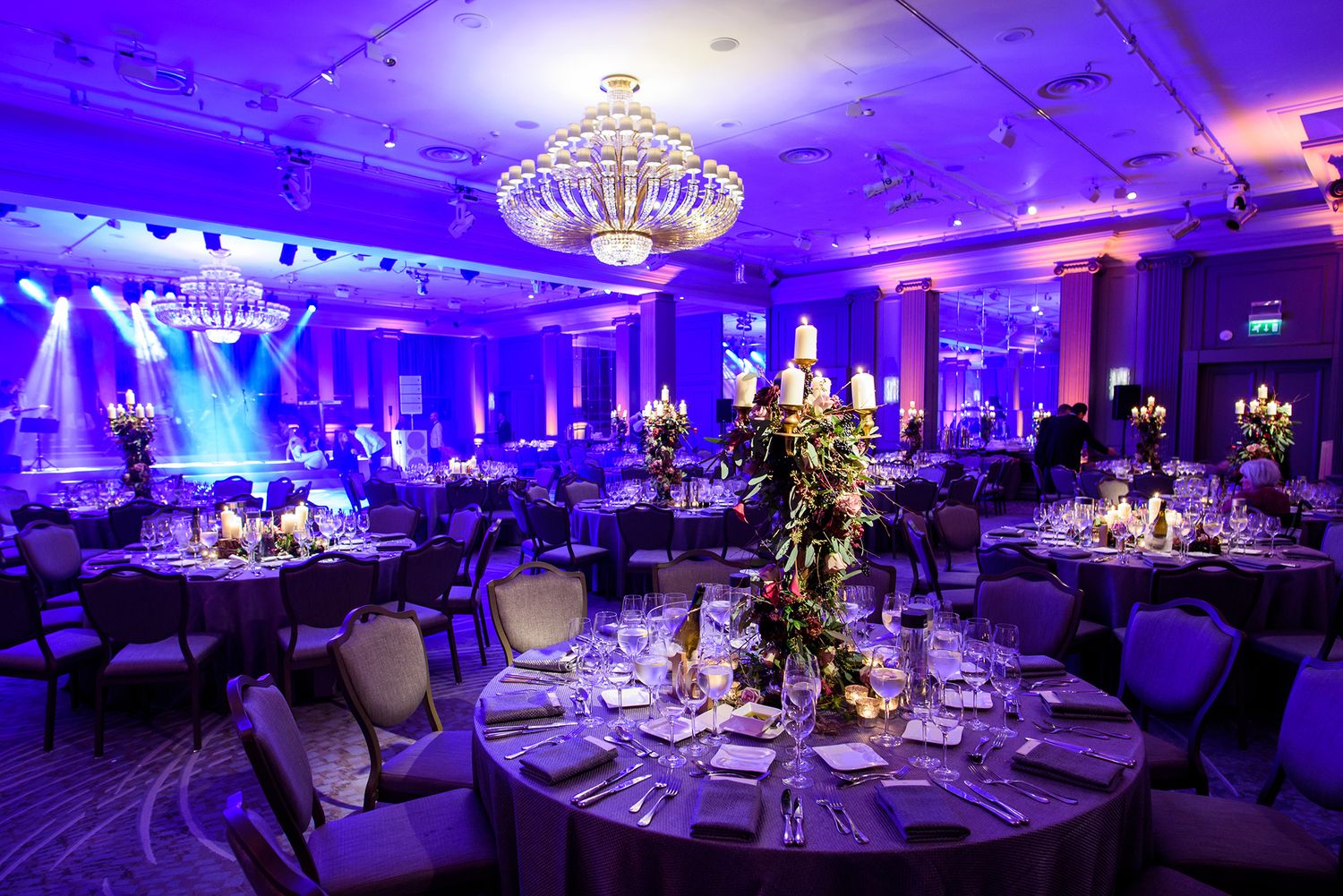 Elegant reception hall with dramatic purple uplighting and crystal chandeliers.