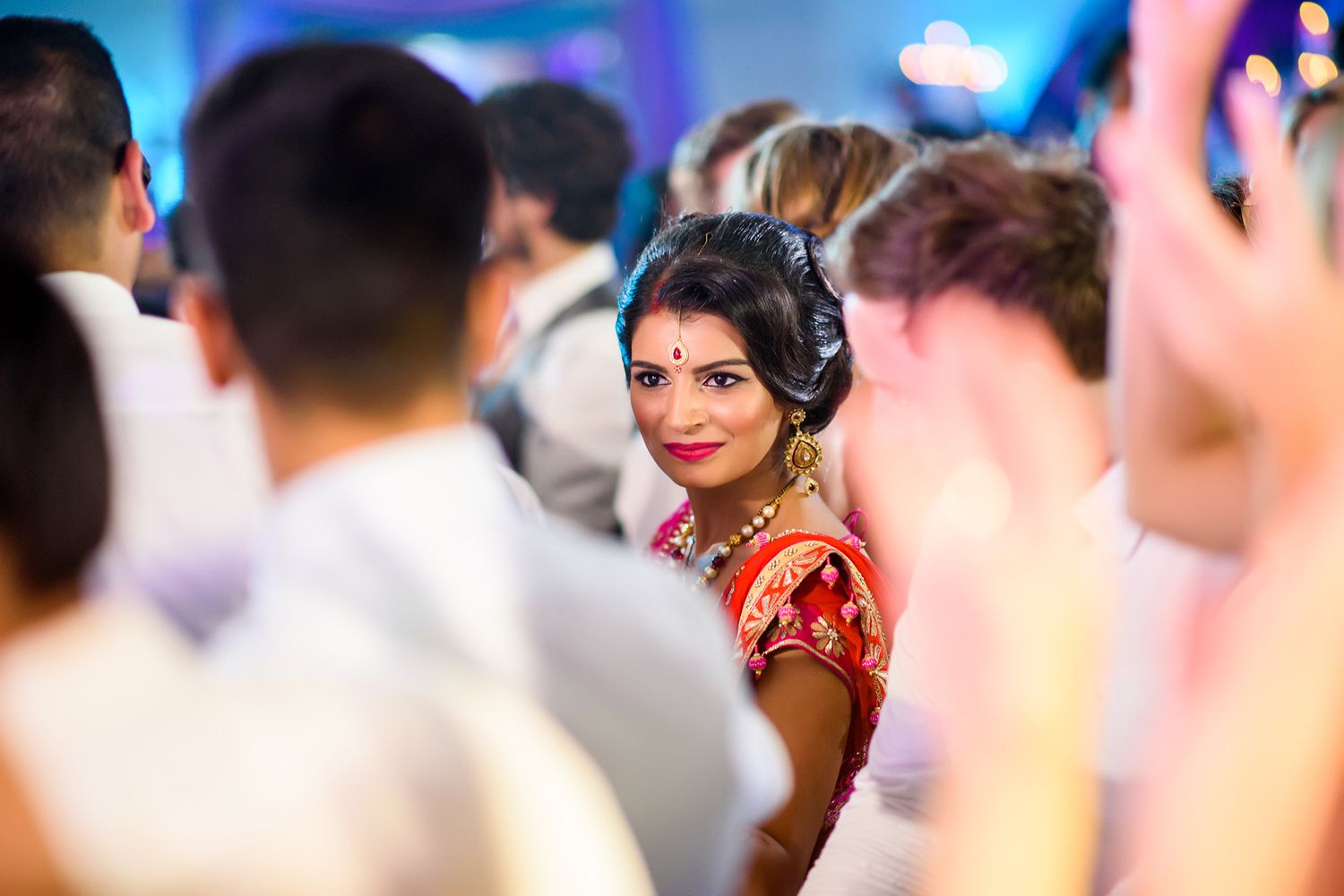 Person in a red traditional dress with headphones looks back amid a crowded dance floor with blue lighting.