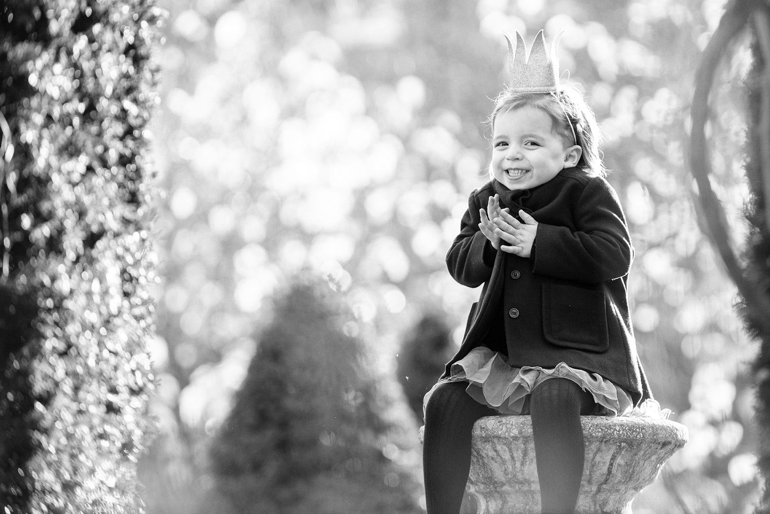 Black and white portrait captured through tree branches with soft bokeh lighting effects.
