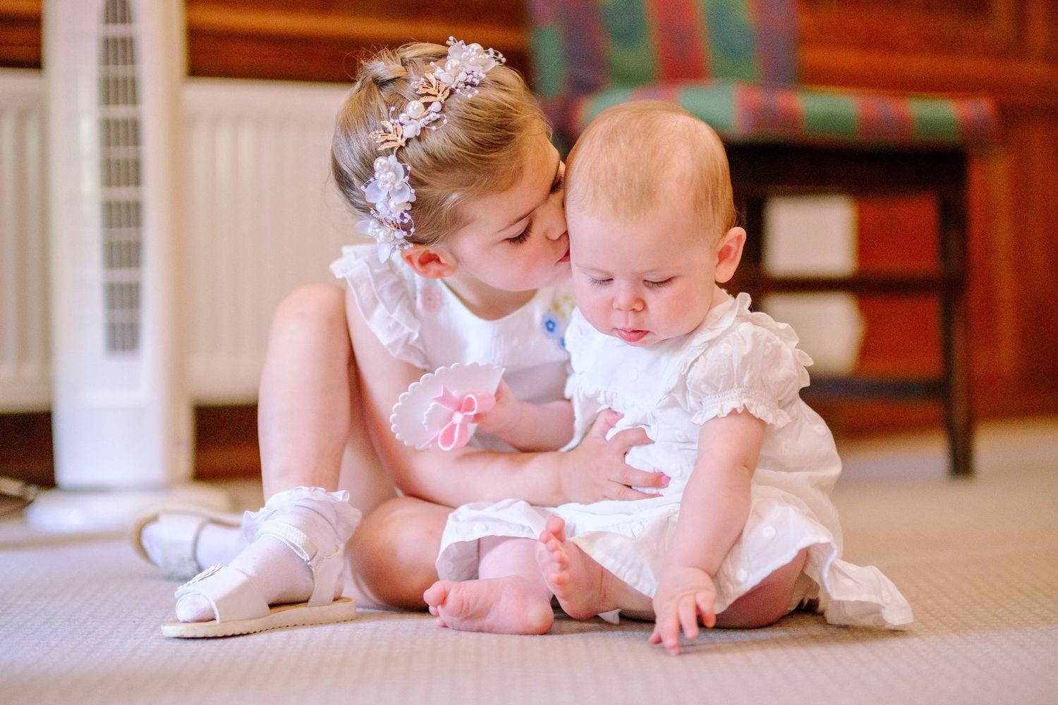 Young children in white dresses playing together on a carpeted floor.