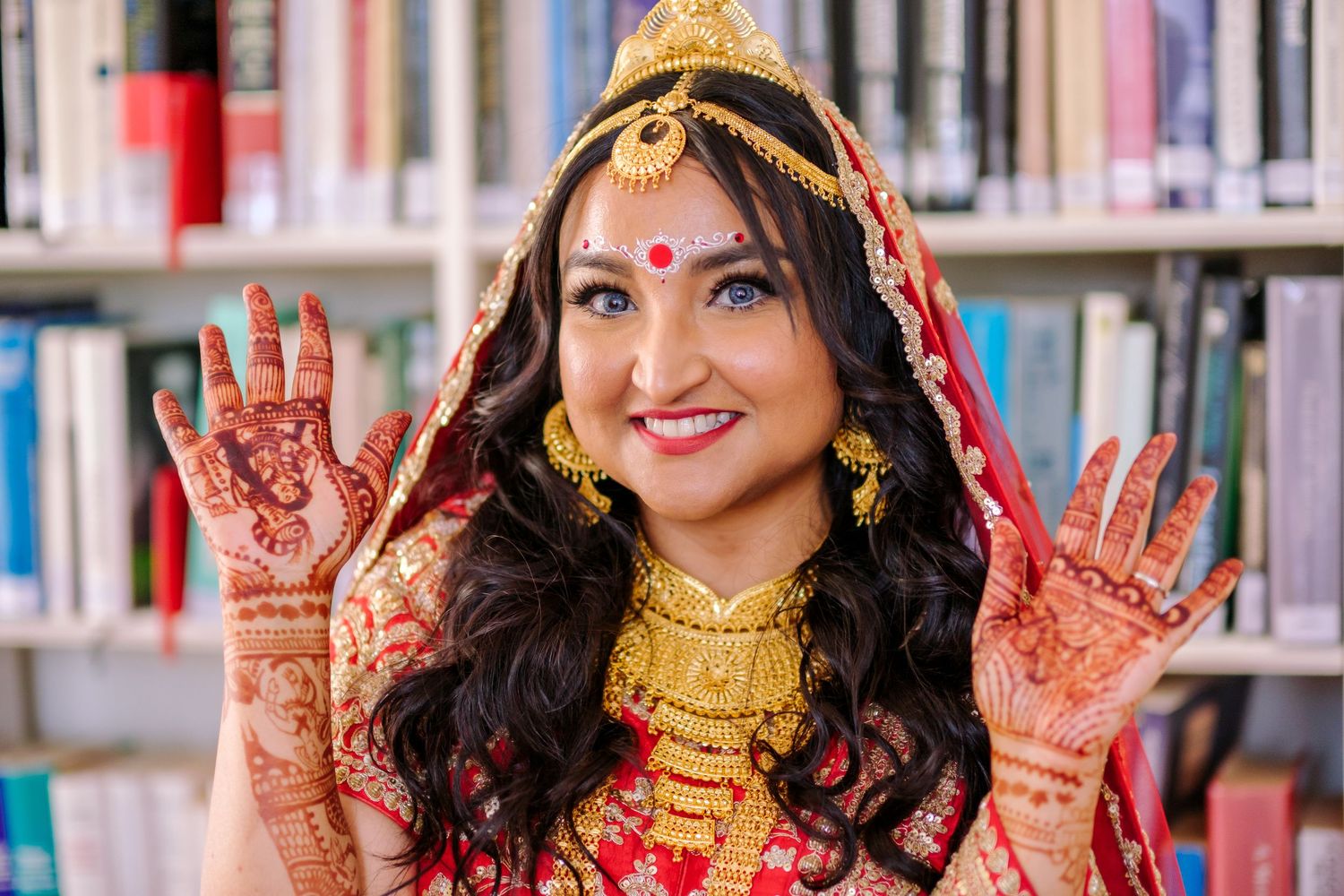 Traditional Indian bride wearing gold jewelry and red bindi displays intricate henna designs on her hands.