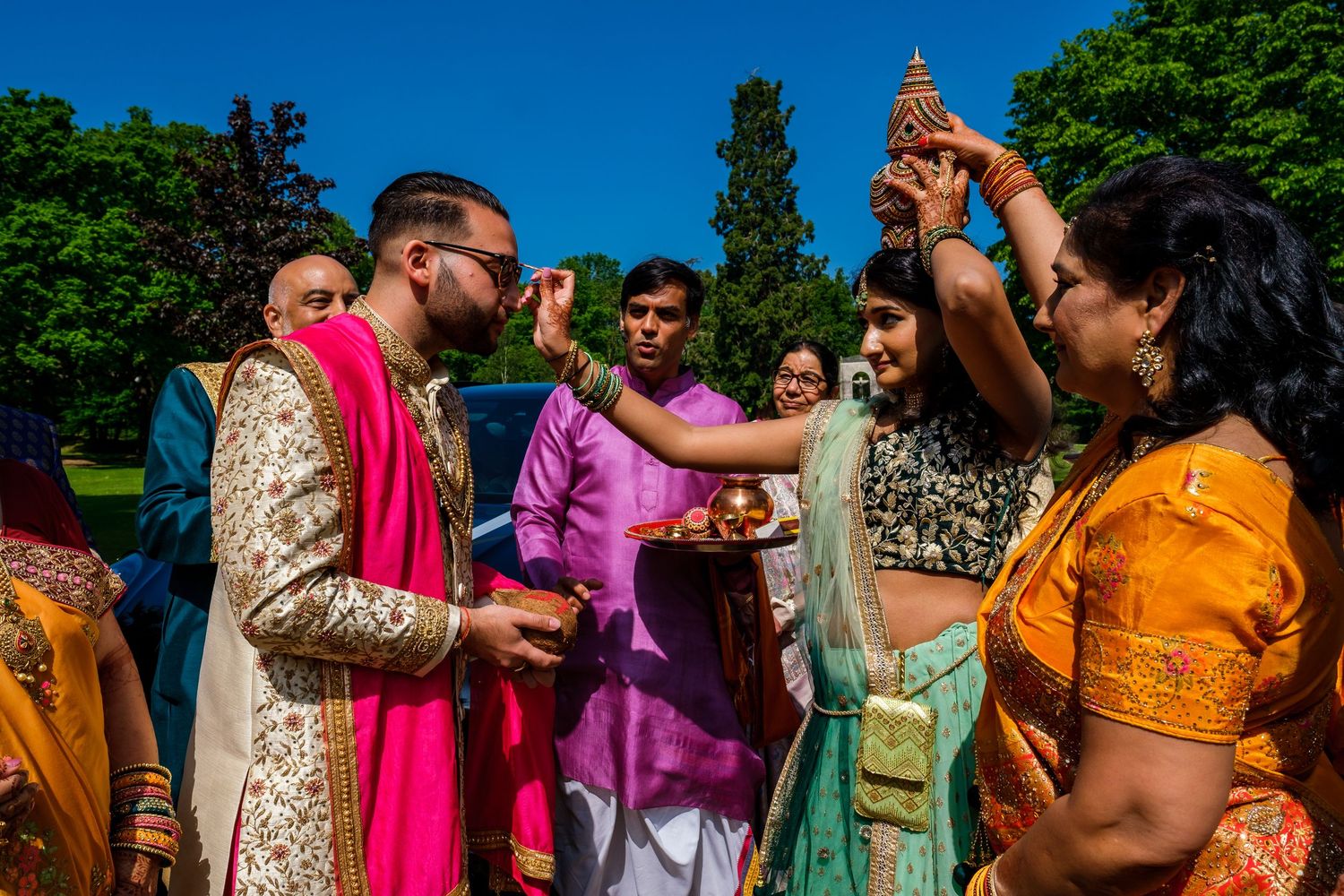 Outdoor gathering with colorful traditional Indian clothing visible against blue sky and trees.